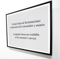 Imagen que muestra un cartel enmarcado, mirado en perspectiva, que pone en español e inglés, “existen hojas de reclamaciones a disposición del consumidor y usuario”.