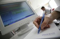 Fotografía que muestra una pantalla de ordenador con información de una factura electrónica, y a un hombre tomando notas en una libreta sobre lo que se está visualizando en el ordenador.