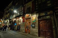 Fotografía en la que se aprecia a un grupo de personas en la calle, frente a la puerta de un bar, de noche. 