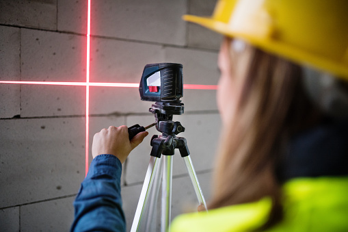 Trabajador joven con el laser en el sitio de edificio.