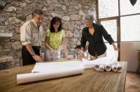 Imagen de tres personas mirando planos extendidos en una mesa.