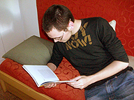 Ricardo con gafas, reclinado en un sofá color rojo, leyendo un libro. 