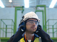  Foto en primer plano de un operario con los equipos de protección individual de casco, protectores auditivos y gafas protectoras.