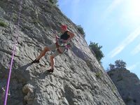 Una escaladora hace rapel sobre una pared de roca, mirando sonriente  a la cámara que la fotografía desde abajo.