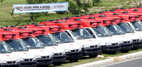 Junto a una carretera se observa una fila de ambulancias aparcadas, junto a una carretera, y detrás de ellas se ve una pancarta desplegada que dice “Mais saúde para a Bahia” (Más salud para Bahía).