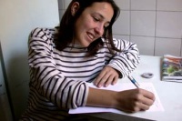 Foto de una joven sonriente, bolígrafo en mano, escribiendo una carta. 