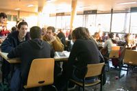 Grupos de estudiantes de edades similares a las de bachillerato sentados en mesas de una cafetería o comedor.