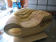 Imagen de un prototipo de sillón diseñado por Silvia Gómez Fernández, realizado en madera de Tulipwood alistonada, y formada por diferentes superficies planas con contorno curvo situadas verticalmente y separadas por piezas de metacrilato de sección circular.