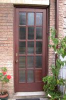 Fotografía de la puerta de entrada posterior de una vivienda, es una puerta de madera con cristales . La fachada des de ladrillo visto.