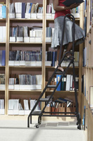 Imagen de una estantería librería de madera llena de archivos y una mujer con una escalera bajando un archivo a la estantería.