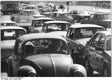 Fotografía en blanco y negro de un atasco, en primer plano aparece un coche "escarabajo", y en segundo plano más coches; de fondo aparecen más coches aún.