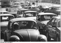 Fotografía en blanco y negro de un atasco, en primer plano aparece un coche "escarabajo", y en segundo plano más coches; de fondo aparecen más coches aún.