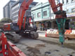 Fotografía en color de una excavadora que tiene un martillo neumático en acción en una calle en obras.