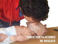 Un alumno practicando las ventilaciones de rescate con un maniquí pediátrico, está insuflando aire por la boca del muñeco. Sobre la foto se puede ver el texto: cinco ventilaciones de rescate.