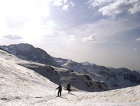 Fotografía de dos montañeros andando por un valle de montaña  nevado.