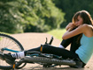 Fotografía de una muchacha que ha caído de su bicicleta. La chica, delgada y con ropa deportiva, está sentada en el suelo sujetándose la rodilla y con expresión de dolor. La bicicleta está tirada entre sus pies.