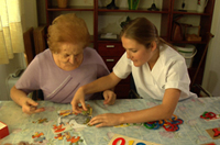 Una persona mayor y una profesional sanitaria ayudándola a hacer un puzzle.