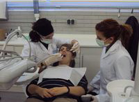 Claudia, recién titulada, observando cómo Elena, técnica con gran experiencia, realiza un tratamiento dental a un paciente en el centro de salud.