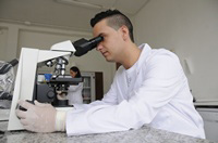 En la imagen se observa a Carlos sentado en frente de un microscopio estudiando un caso. 