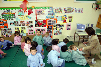 Fotografía que muestra a una educadora junto a un montón de niñas y niños en un aula infantil.