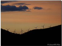 Fotografía, en la penumbra del atardecer, del contorno de una montaña con molinos de producción de energía eólica.