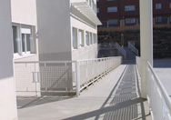 Se ve la rampa de entrada  para minusválidos de un colegio. Es un edificio completamente blanco.
