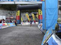 Meta de una carrera de atletismo, con vallas publicitarias,  y un corredor atravesando la meta a la carrera. 