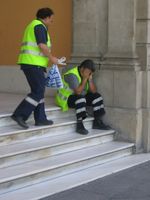 Dos empleados de emergencias en una escalinata, uno sentado con las manos en la cara, en actitud afligida, y el otro de pie, en actitud de ir a tenderle.