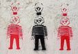 Se ven tres muñecos, que parecen de playmobil,  pintados en una pared, con un spray usando la mima plantilla,   cada uno con una bombilla encima. Los dos de los lados en rojo, y el del centro en negro. 