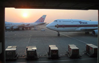 Se ven dos grandes aviones en la terminal de un aeropuerto, con el sol brillando encima, entre la bruma. 