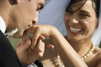Una pareja joven  en su boda, el hombre besa la mano dela novia y ella sonríe.