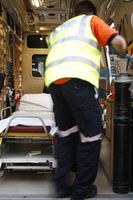 Técnico en emergencias de espaldas con una ambulancia abierta al fondo.