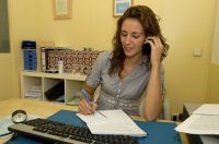 María sentada, trabajando mirando hacia su escritorio, con folios y un teclado de ordenador sobre la mesas.
