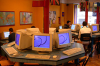 Sala con mesas y ordenadores sobre ellas, parece ser un aula de informática o cibercafé.