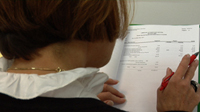 Ada de espaldas trabajando con papel y bolígrafo.