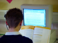 Estudiante sentado de espalda trabajando con ordenador y un libro.