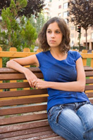 Foto de Ana  sentada en un banco de un parque, mirando al frente y pensativa.