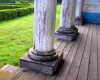 Se visualiza la base de unas columnas de piedra sobre suelo de madera en exterior.