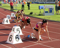 En una pista de atletismo, desde la calle seis a la calle uno, varias atletas se encuentran en los tacos preparadas para comenzar la carrera.