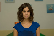 Imagen de una mujer joven, de frente, seria, con pelo suelto, castaño a la altura de los hombros, camiseta azul de manga corta.